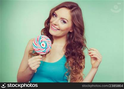 Woman attractive cheerful girl holding colorful lollipop candy in hand. Sweet food and enjoying concept. Studio shot green blue background, toned image. Smiling girl with lollipop candy on teal