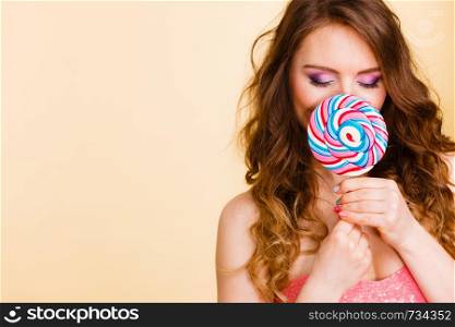 Woman attractive girl colorful eyes make up holding big lollipop candy in hand, covering her face. Sweet food and enjoying concept. Studio shot on bright. Woman holds colorful lollipop candy in hand, covering face