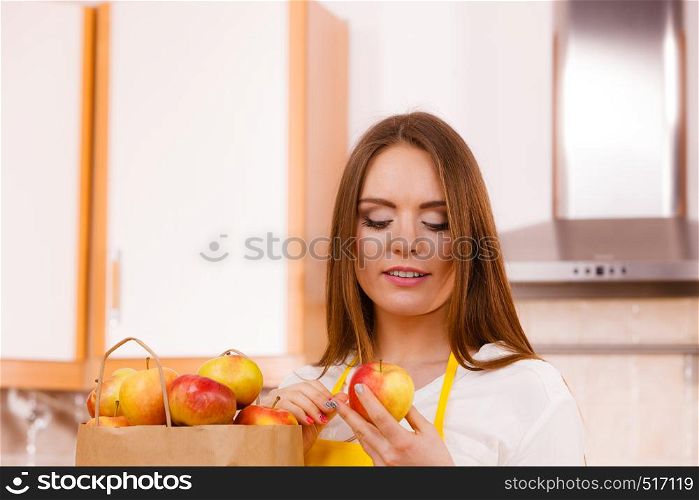 Woman attractive housewife in kitchen with grocery shopping bag, many apple fruits. Healthy eating, cooking, vegetarian food, dieting and people concept.. Woman housewife in kitchen with many fruits