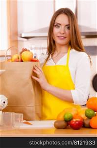 Woman attractive housewife in kitchen with grocery shopping bag, many fruits on counter. Healthy eating, cooking, vegetarian food, dieting and people concept.. Woman housewife in kitchen with many fruits 