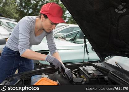 woman auto mechanic fixing the engine of a car outdoors
