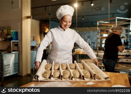 Woman baker preparing sweet buns pastries with sesame seeds while working at professional kitchen of modern bakery house. Woman baker preparing sweet buns pastries with sesame seeds