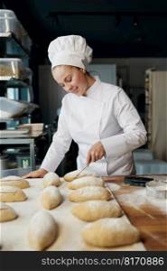 Woman baker wearing uniform engaged in decorating of traditional yeast buns. Woman baker decorating traditional yeast buns