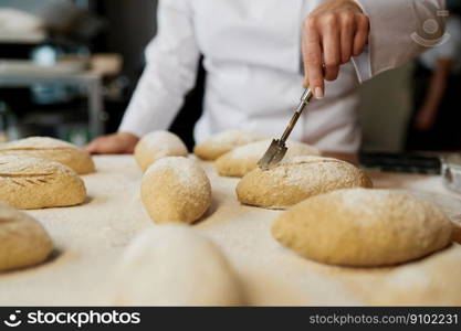 Woman baker wearing uniform engaged in decorating of traditional yeast buns. Closeup view. Woman baker decorating traditional yeast buns