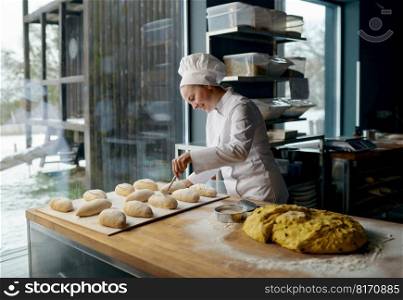 Woman baker wearing uniform engaged in making of traditional yeast buns with cheese. Baker engaged in making of traditional yeast buns with cheese