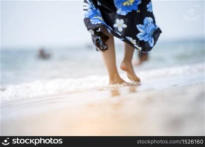 Woman bare foot walking on summer beach. close up leg of young woman walking along wave of sea water and sand on vacation beach. Enjoyment barefoot walk outdoor with freedom. Relaxation Travel Concept.