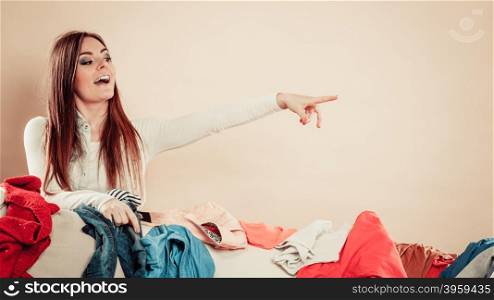 Woman behind sofa full of clothes point with finger.. Lifestyle and decisions about outfit. Houshold and laundry. Young female behind sofa full of clothes. Woman point away with finger.