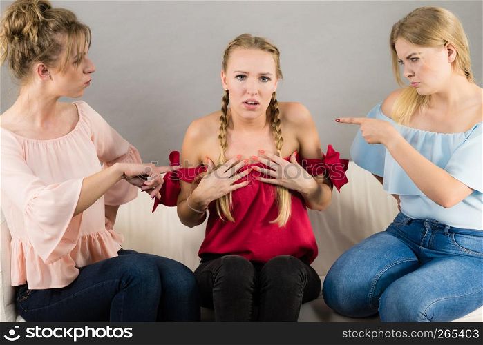 Woman being bullied by her two female friends. Females pointing blaming at friend. Friendship rivaly and envy problems.. Woman being bullied by two females