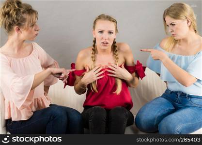 Woman being bullied by her two female friends. Females pointing blaming at friend. Friendship rivaly and envy problems.. Woman being bullied by two females