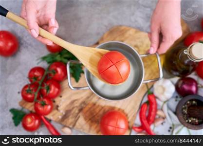 woman blanching a tomato holding over pan with hot water for further peeling.. woman blanching a tomato holding over pan with hot water for further peeling