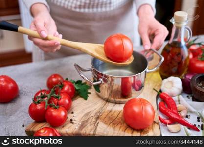 woman blanching a tomato holding over pan with hot water for further peeling.. woman blanching a tomato holding over pan with hot water for further peeling