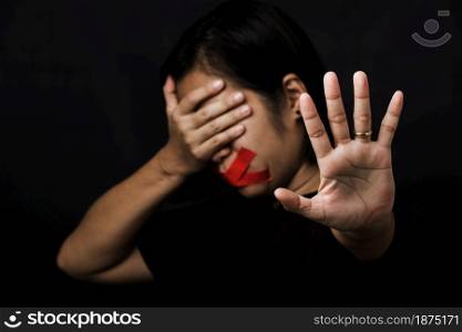 Woman blindfold wrapping mouth with red adhesive tape and show hand sign stop abusing violence and abuse on black background, Human trafficking and abuse, International Human Rights day