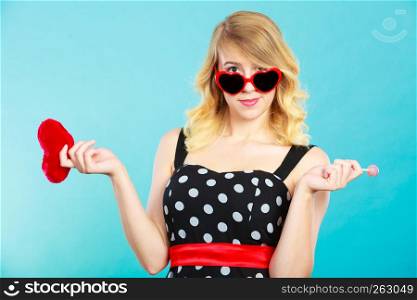 Woman blonde lovely girl wearing dotted dress holding red heart love symbol and lollipop candy. Valentines day, happiness, sweet food concept. Woman holds red heart love symbol and lollipop candy