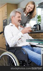 Woman Bringing Man In Wheelchair Hot Drink At Home