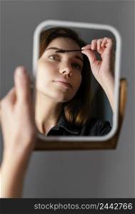 woman brushing her eyebrows while looking mirror after treatment