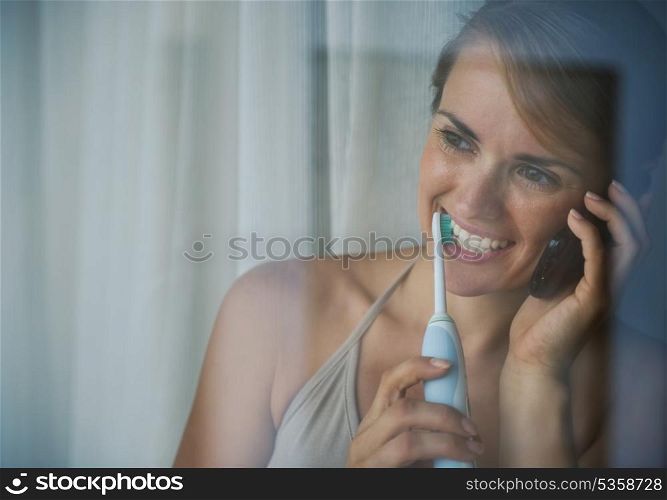 Woman brushing teeth with electric toothbrush and speaking mobile