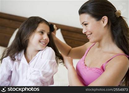 Woman brushing young girl&acute;s hair on bed in bedroom smiling (selective focus)