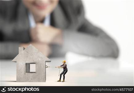 Woman builder. Businesswoman looking at miniature of builder pulling house model