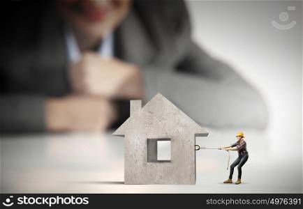 Woman builder. Businesswoman looking at miniature of builder pulling house model