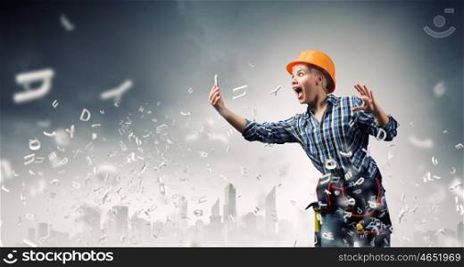 Woman builder in anger. Young emotional woman mechanic screaming in mobile phone
