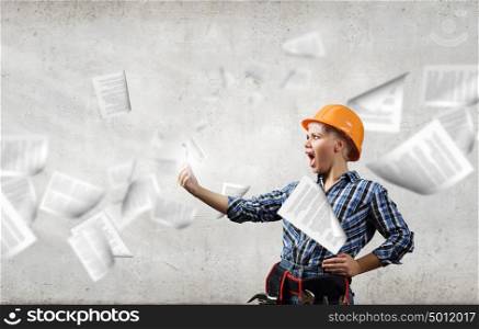 Woman builder in anger. Young emotional woman mechanic screaming in mobile phone