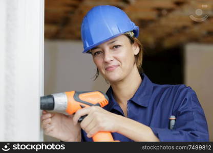 woman builder working with driller and window