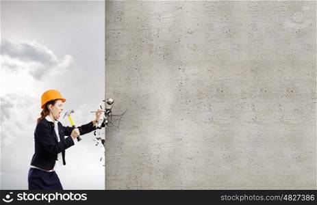 Woman builder. Young woman in business suit hitting hobnail with hammer