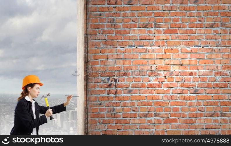 Woman builder. Young woman in business suit hitting hobnail with hammer