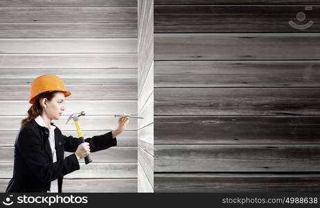 Woman builder. Young woman in business suit hitting hobnail with hammer