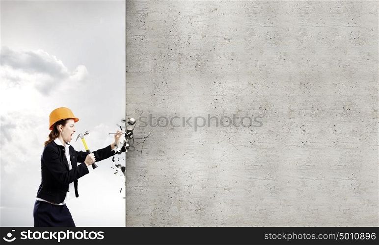 Woman builder. Young woman in business suit hitting hobnail with hammer