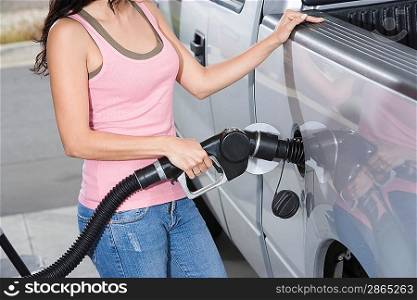 Woman by car with fuel pump, mid section