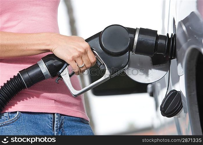 Woman by car with fuel pump, mid section