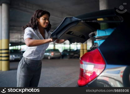 Woman can’t close the trunk with suitcases, car parking. Female traveler packs luggage, vehicle park lot, passenger with many bags. Girl with baggage near automobile. Woman can’t close trunk with suitcases, parking