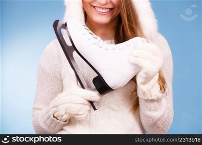 Woman carrying a pair of ice skates getting ready for ice skating, winter sport activity, on blue. Woman holding ice skates