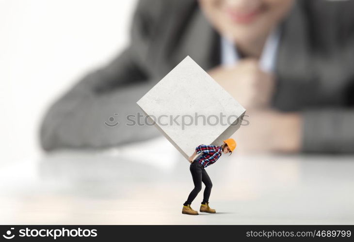 Woman carrying cube. Businesswoman looking at miniature of woman builder carrying white cube
