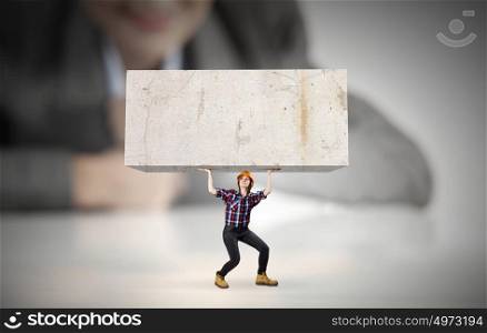 Woman carrying cube. Businesswoman looking at miniature of woman builder carrying white cube