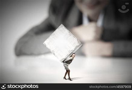 Woman carrying cube. Businesswoman looking at miniature of woman carrying white cube on back