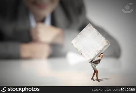 Woman carrying cube. Businesswoman looking at miniature of woman carrying white cube on back