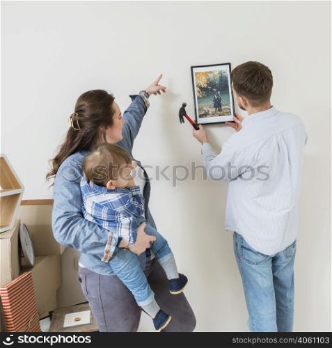 woman carrying his son directing his husband fix frame wall