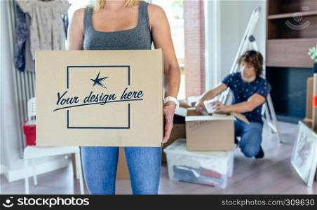 Woman carrying moving box while her husband unpacks. Customizable box design. Woman carrying moving box