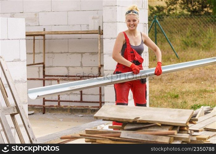 Woman carrying steel metal made gutter on her house construction site, building new home, fixing hydraulics. Woman carrying gutter on construction site