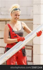 Woman carrying steel metal made gutter on her house construction site, building new home, fixing hydraulics. Woman carrying gutter on construction site