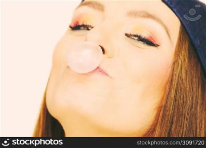 Woman casual style teen girl cap on head colorful makeup doing bubble with chewing gum closeup. Youth style. Woman doing bubble with chewing gum