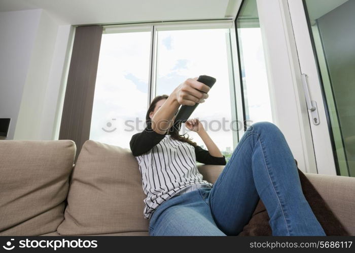 Woman changing channels while watching TV on sofa at home