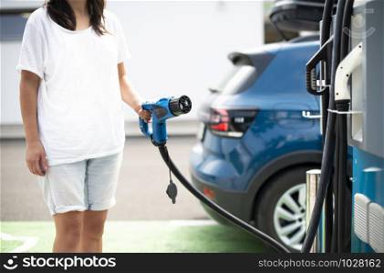 Woman charge her Electric car on gas station. Blue car and electric plug for charging. Ecology fuell concept.