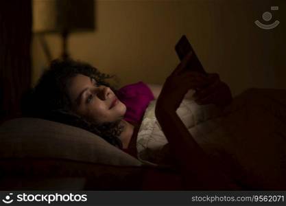 Woman Chatting on smartphone at night while lying on bed 