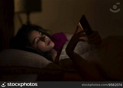 Woman Chatting on smartphone at night while lying on bed 