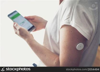 Woman checking glucose level with a remote sensor and mobile phone, sensor checkup glucose levels without blood. Diabetes treatment.