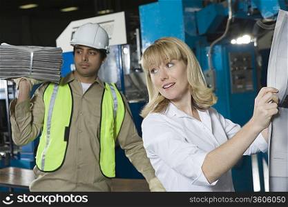 Woman checking newspaper in factory with colleague in background