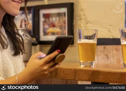 Woman checks her smartphone while enjoying a beer